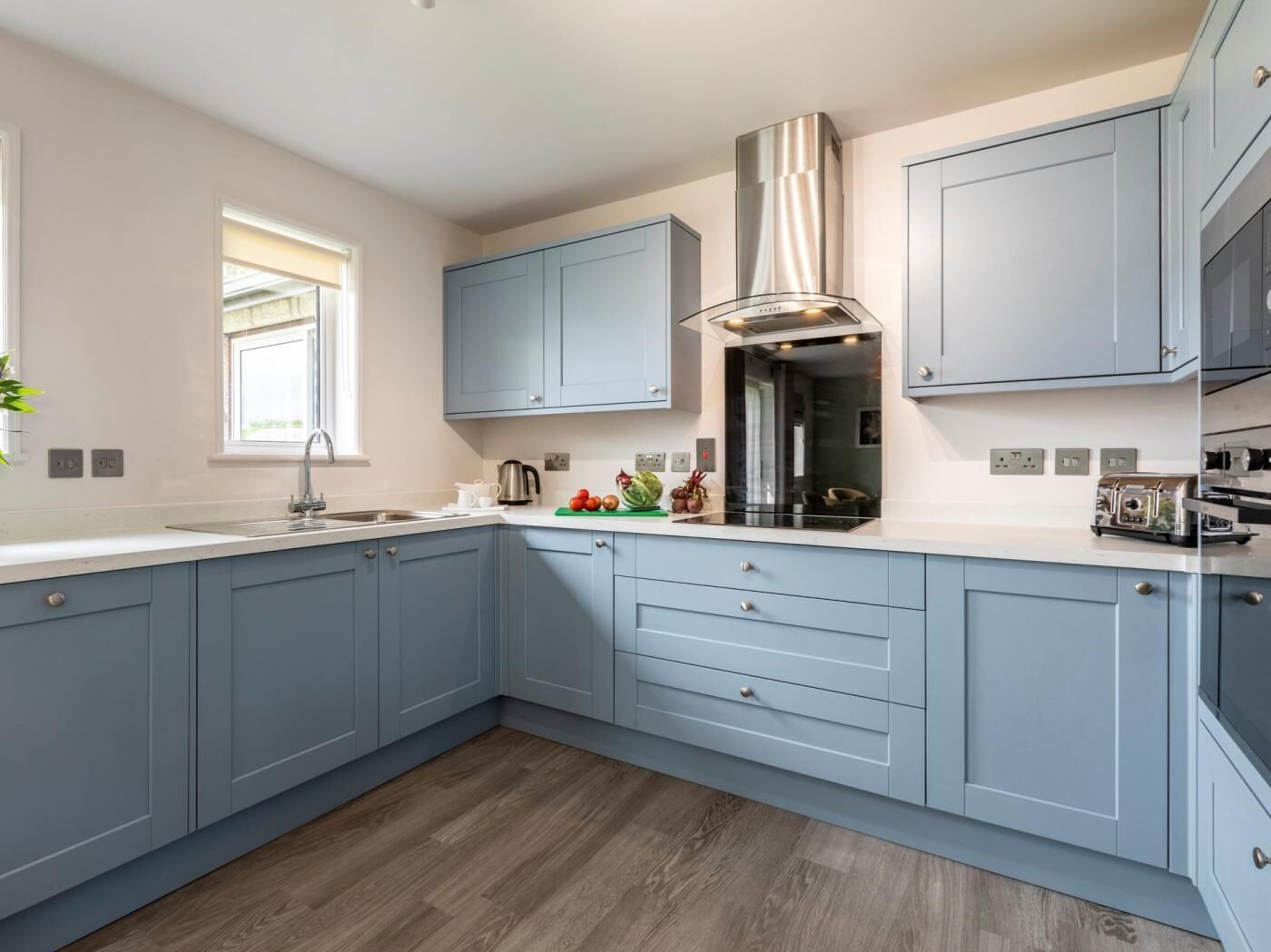 A modern kitchen with light blue cabinets, a stainless steel range hood, and a window providing natural light.