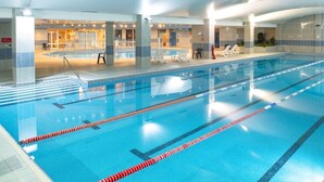 Una piscina interior con carriles delimitados, una zona de descanso con sillones y un mostrador de recepción.