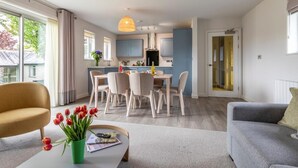 Una sala de estar moderna con comedor, una cocina con armarios azules y un ventanal con cortinas.
