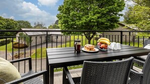 Een balkon met een ontbijtset, een boom en een gebouw op de achtergrond.