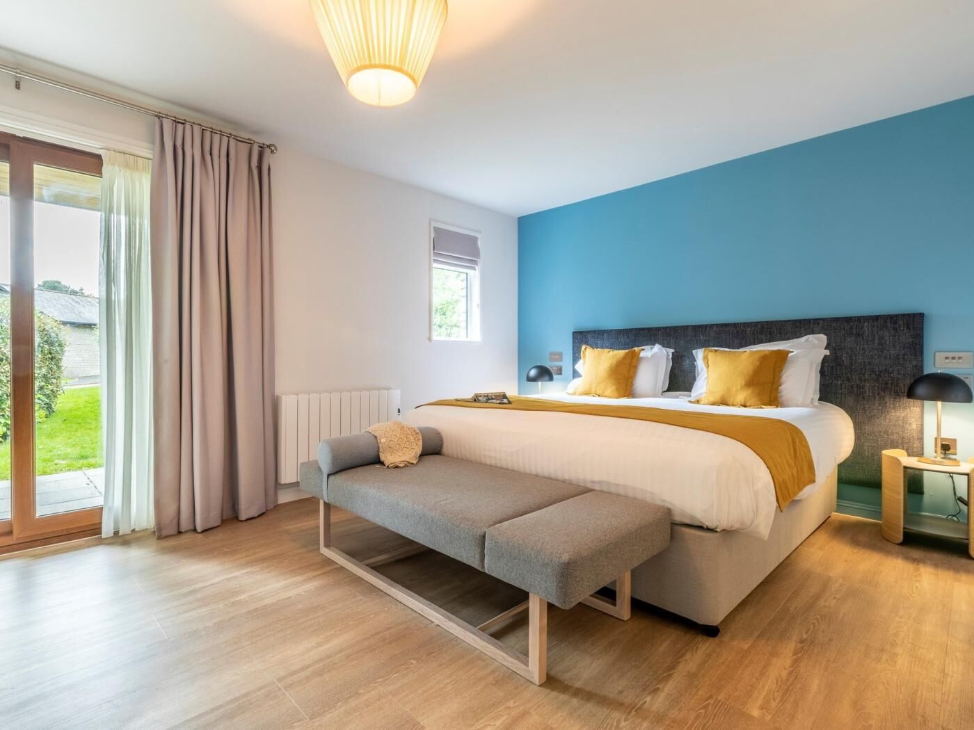 Een slaapkamer met een bed, een bankje, een nachtkastje, een lamp en uitzicht op het omliggende landschap.