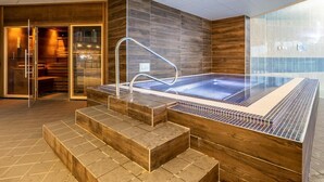 Ett modernt spaområde med ett bubbelbad, trästeg och en glasdörr som leder till en sittgrupp.