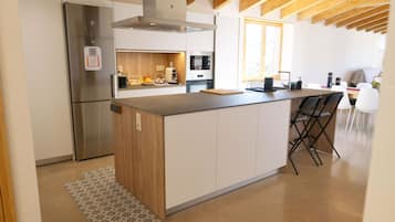 A modern kitchen with a central island, stainless steel appliances, and a wooden ceiling.