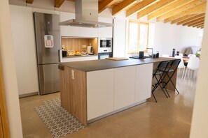A modern kitchen with a central island, stainless steel appliances, and a wooden ceiling.