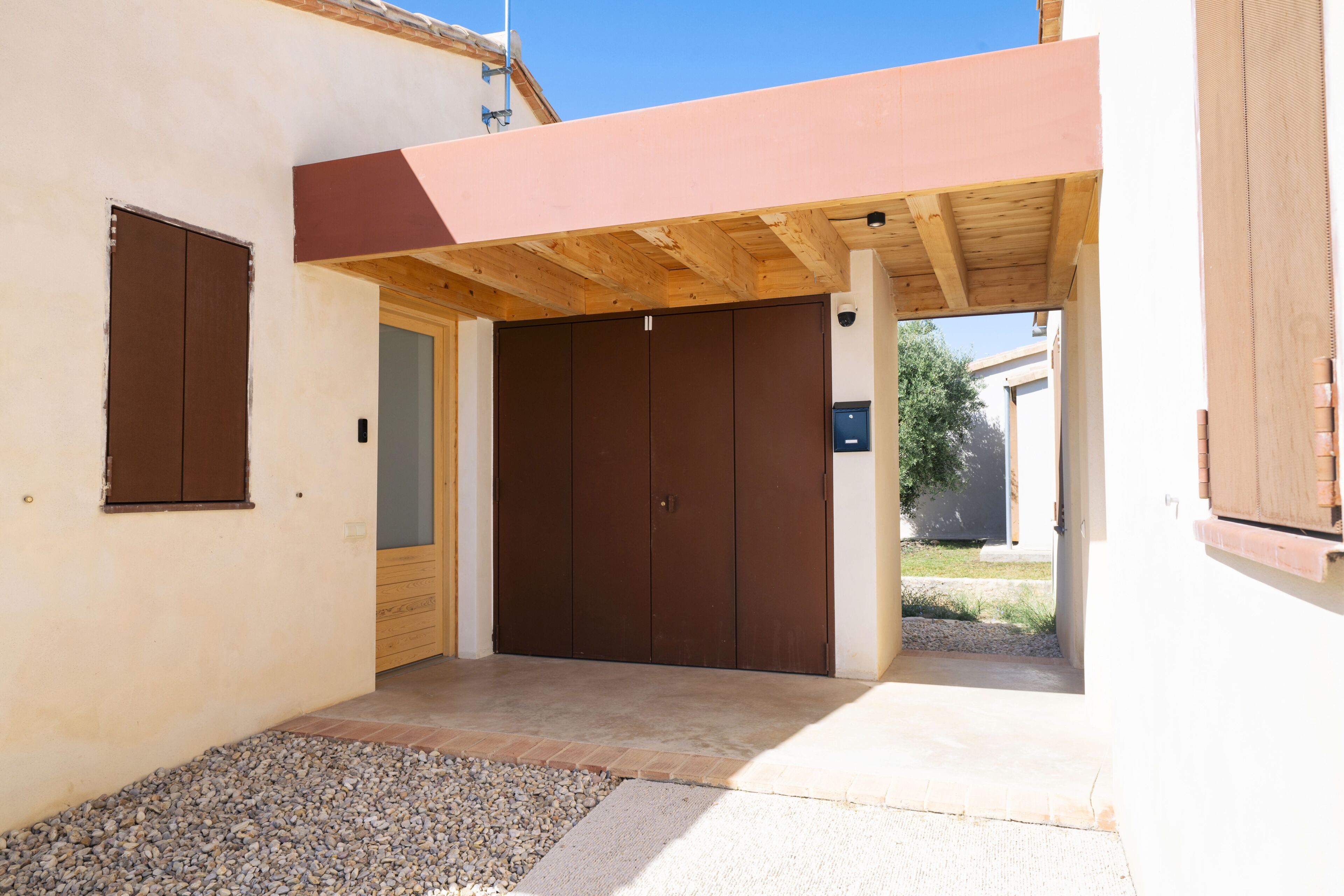 A covered outdoor entrance with a wooden ceiling, a brown door, and a small gravel area.