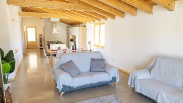 Un salon moderne avec un plafond en bois, un canapé gris et un coin repas à l’arrière-plan.
