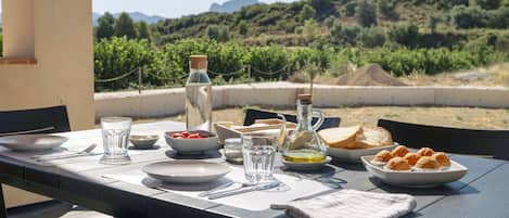 A table set outdoors with plates, glasses, a bottle, and food items.