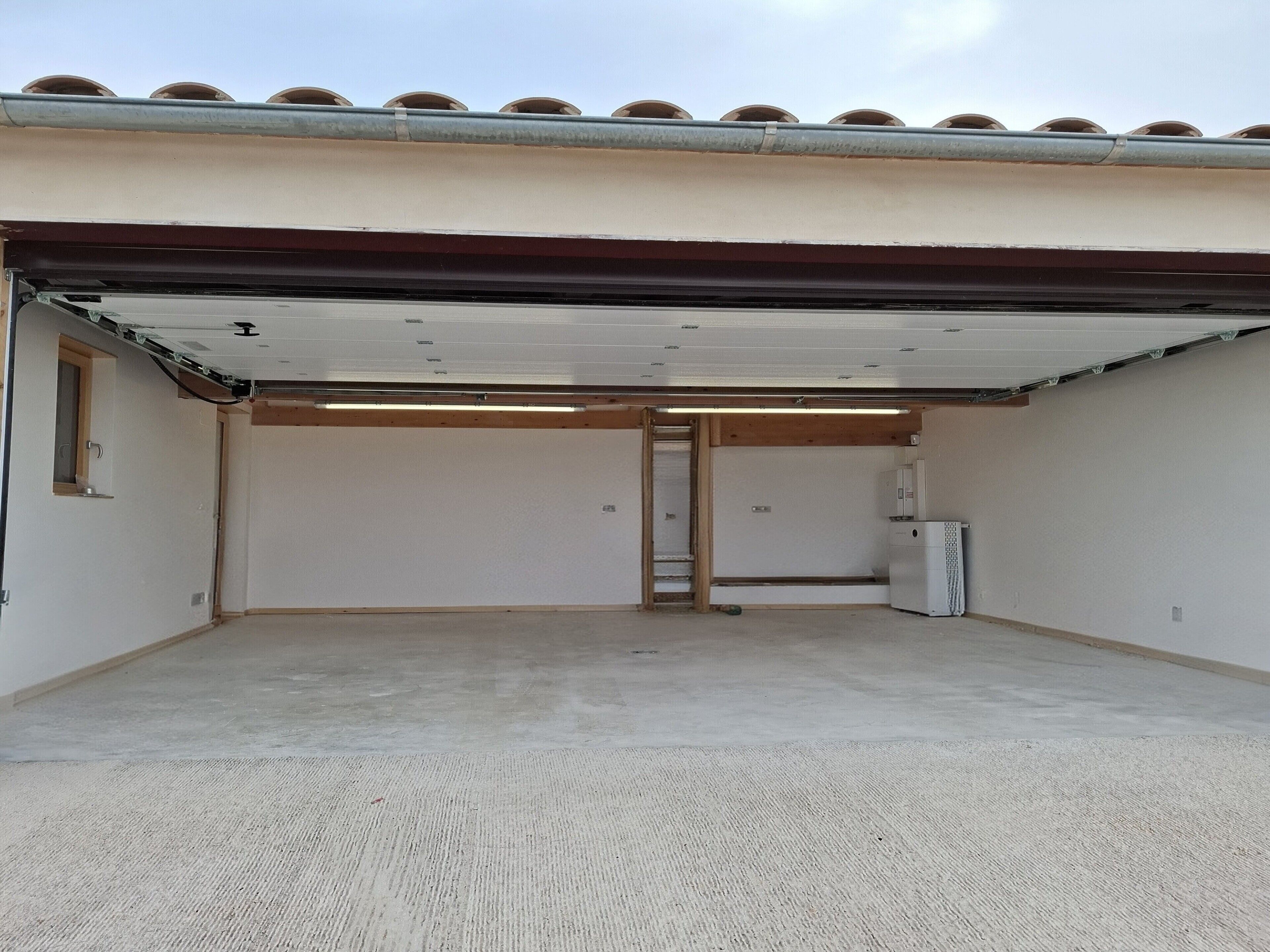 Un garaje con piso de concreto, puerta blanca y rejilla metálica.