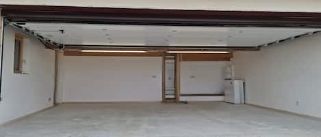 Un garage avec un plancher en béton, une porte blanche et une grille de ventilation en métal.