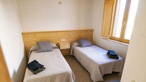 A room with two single beds, each with a pillow and a folded towel.