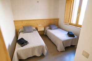 Une chambre avec deux lits simples, chacun étant équipé d’un oreiller et d’une serviette pliée.