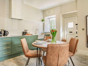 Une cuisine moderne avec des meubles de couleur verte, une table de salle à manger ronde et deux chaises.