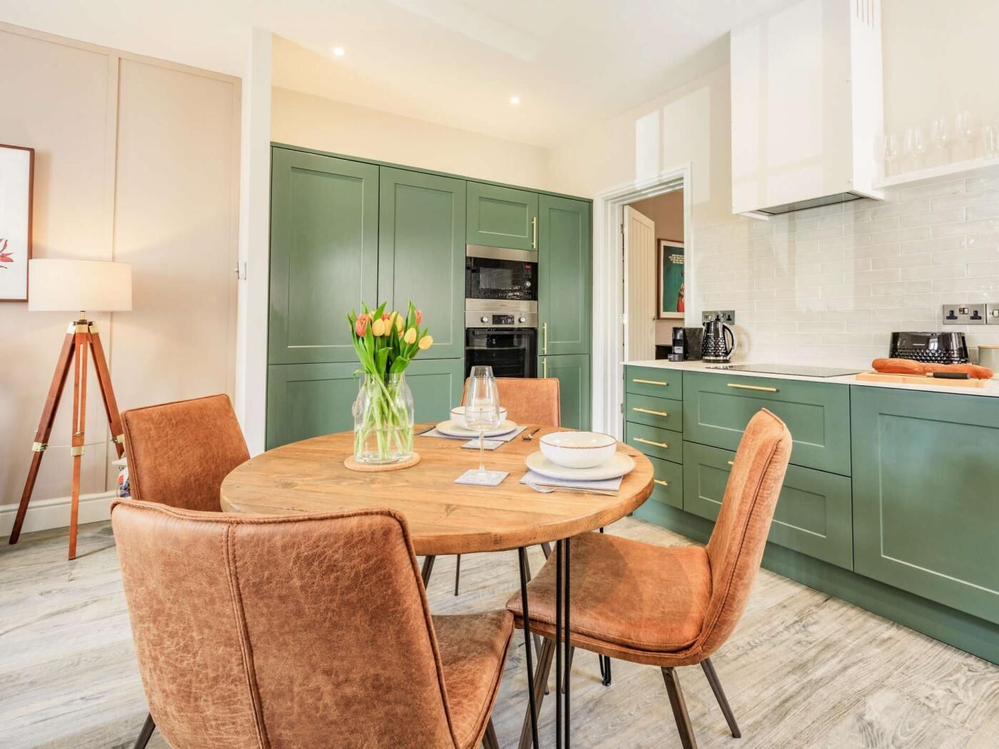 Een moderne keuken met groene kastjes, een eettafel met stoelen en een vaas vol tulpen.