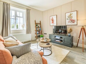 Ein Wohnzimmer mit einer Couch, einem Couchtisch, einem Bücherregal, einem Fernseher und einem Stativ.