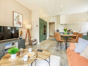 Un salon moderne avec un téléviseur, un coin repas avec des chaises et une table, et une cuisine équipée de placards et d’un évier.