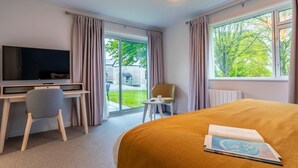 A hotel room with a bed, a desk with a TV, a chair, and a view of the outdoors. - 2 Bed in Saltash (oc-87713) (Saint Mellion)