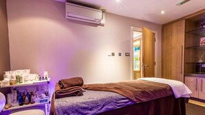 A room with a bed, a massage table, a shelf with toiletries, and an air conditioning unit. - 2 Bed in Saltash (oc-87713) (Saint Mellion)