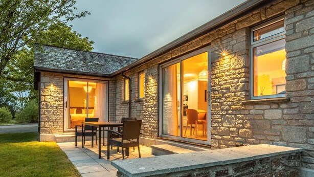 A stone house with a patio, a dining area, and a kitchen visible through glass doors. - 2 Bed in Saltash (oc-87713) (Saint Mellion)