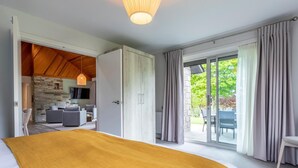 A bedroom with a large bed, a stone wall, a dining area, and a view of the outdoors. - 3 Bed in Saltash (oc-87711) (Saint Mellion)
