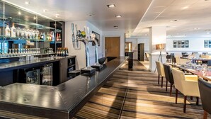 A modern bar area with a long counter, multiple taps, and a variety of bottles. There is a dining area with tables and chairs in the background. - 2 Bed in Saltash (oc-87705) (Saint Mellion)