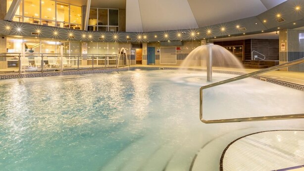 An indoor swimming pool with a water fountain, glass railings, and a modern architectural design. - 2 Bed in Saltash (oc-87705) (Saint Mellion)