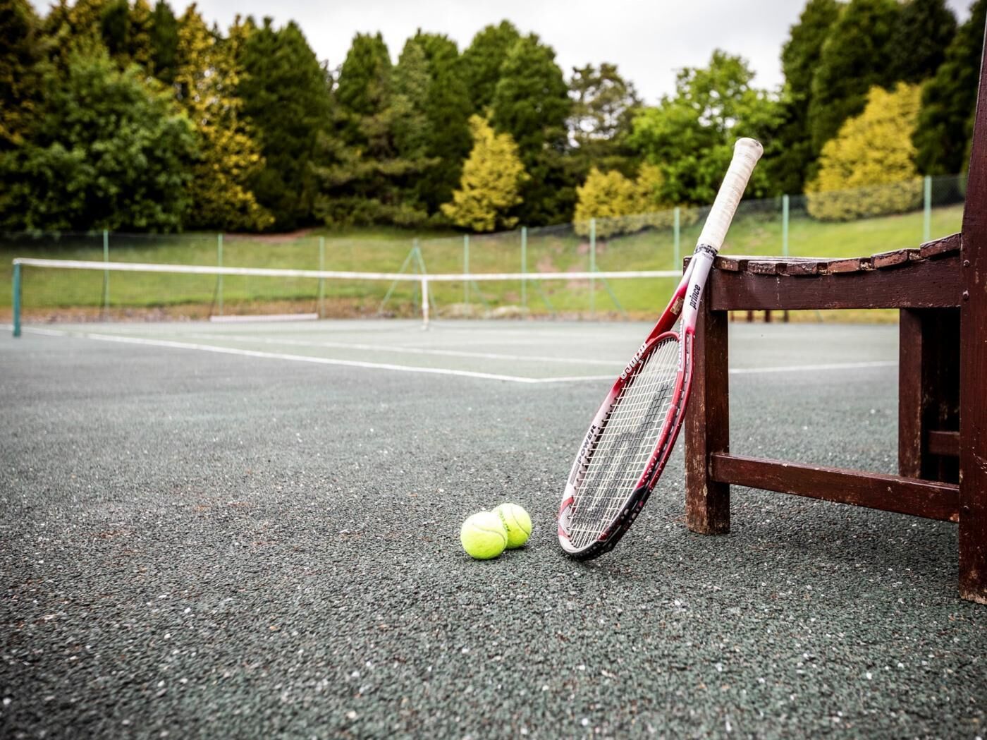 Ein Tennisplatz mit Netz, ein Tennisball und ein Schläger, der an einem Holzpfosten angelehnt ist.