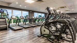 Uma academia com esteiras, bicicletas ergométricas e uma grande janela com vista para o exterior.