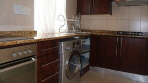 Een keuken met een ingebouwde wasmachine en droger, houten kastjes, een roestvrijstalen fornuis en een raam met gordijnen.