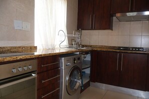 Een keuken met een ingebouwde wasmachine en droger, houten kastjes, een roestvrijstalen fornuis en een raam met gordijnen.