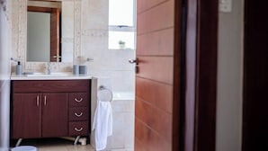 Een badkamer met een houten wastafelmeubel, een spiegel, een handdoekhouder en een raam.