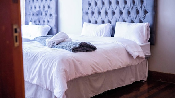 Een tweepersoonsbed met een gestoffeerd hoofdbord, wit beddengoed en een opgevouwen deken.