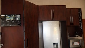 Een keuken met een ingebouwde koelkast, houten kastjes, een magnetron en een digitaal scherm.