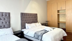 Een moderne slaapkamer met twee bedden, een houten garderobe en een klein tafeltje.
