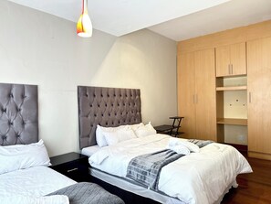 A modern bedroom with two beds, a wooden wardrobe, and a small table. - Room-luxurious Room - C (Johannesburg)