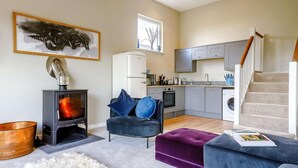 Un salon moderne avec une cheminée, un canapé, un pouf et une cuisine en arrière-plan.