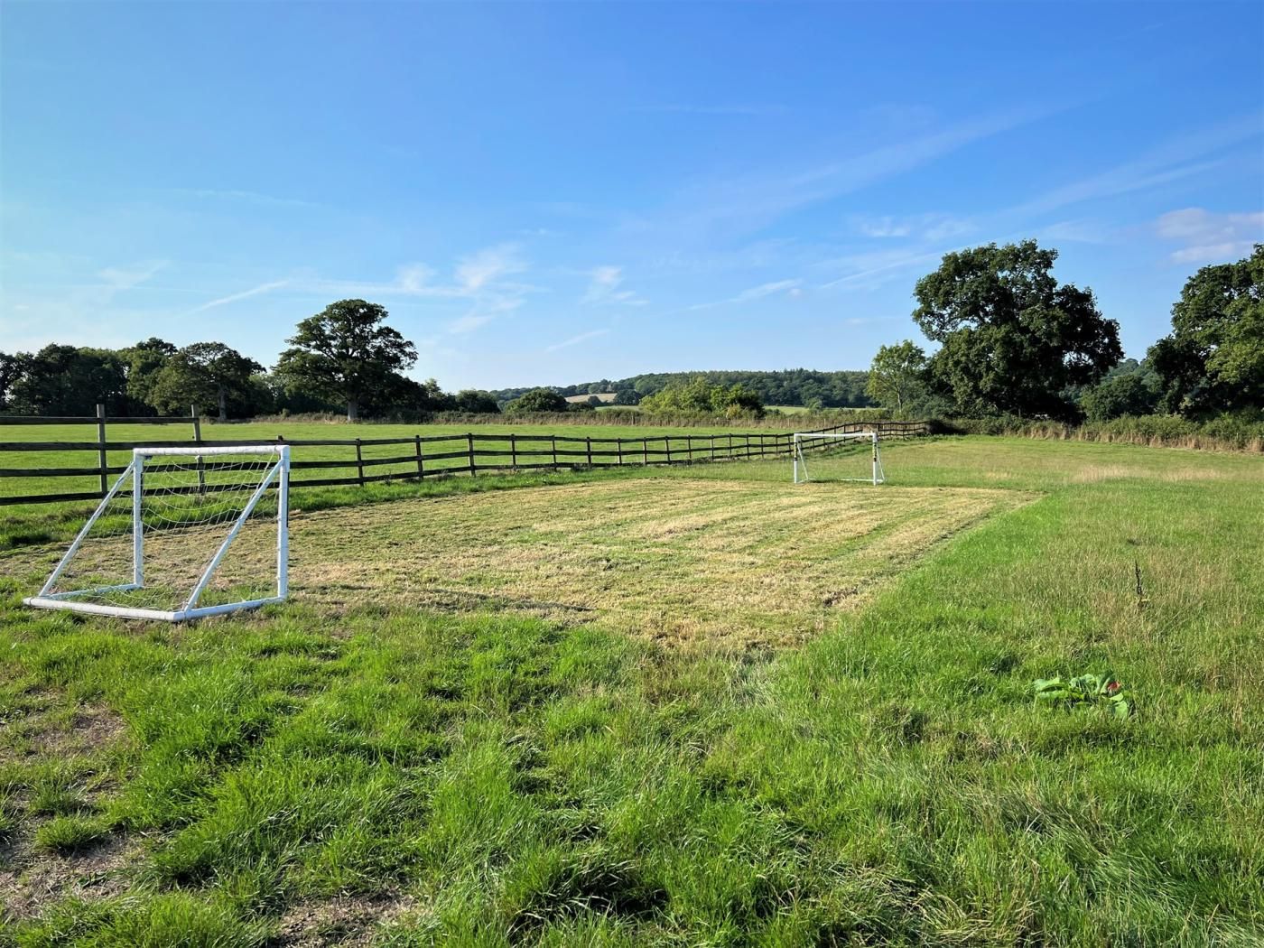 A grassy field with a soccer goal and a wooden fence.