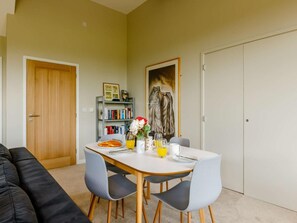 A dining area with a table set for two, a bookshelf, and a painting on the wall.