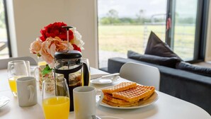 Une table mise pour le petit-déjeuner avec des gaufres, une machine à café et un vase de fleurs.