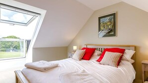 Une chambre avec un plafond en pente, un lit avec une literie blanche et des oreillers rouges, une table de chevet avec une lampe, et un tableau accroché au mur.