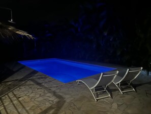 Une piscine recouverte d’une bâche bleue, avec un revêtement de sol en pierre et deux chaises longues.