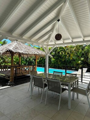 A covered outdoor area with a pool, a thatched structure, and a table with chairs. - Villa Rafaela, Private Pool and Garden (Saint-François)