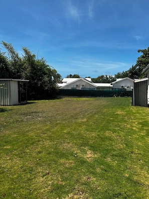 A grassy yard with a fenced area, a small shed, and a larger building with a sloped roof. - Villa Rafaela, Private Pool and Garden (Saint-François)