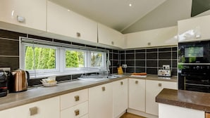 A modern kitchen with white cabinets, a black backsplash, and a window overlooking greenery. - 2 Bed in Barnstaple (oc-87360) (Kentisbury)