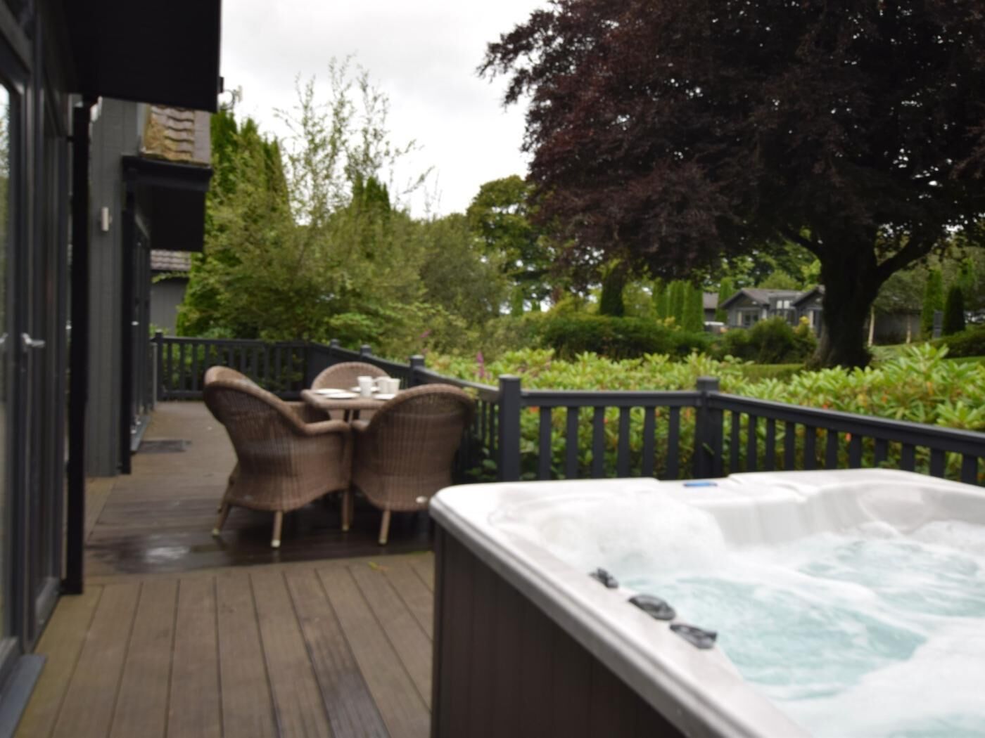 A wooden deck with outdoor furniture, a hot tub, and a view of a garden and houses.