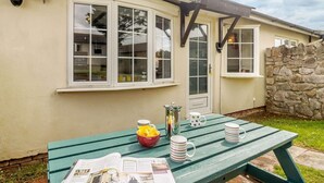 A house with a stone wall, a green picnic table with newspapers, and a window with a view. - 2 Bed in Brixham (oc-88279) (Brixham)