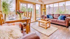 A spacious living room with a high ceiling, large windows, a wooden dining table set, a leather sofa, and a coffee table. - 2 Bed in Morpeth (oc-88270) (Rothbury)