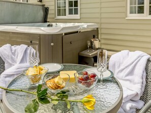 A glass table with food items and drinks, a rose, and a hot tub in the background. - 1 Bed in Cinderford (oc-88272) (Cinderford)