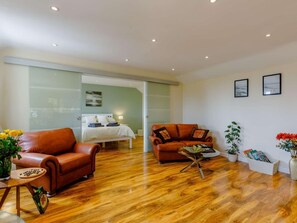 A modern living room with a sofa, a coffee table, and a bed in the background. - 1 Bed in Cinderford (oc-88272) (Cinderford)