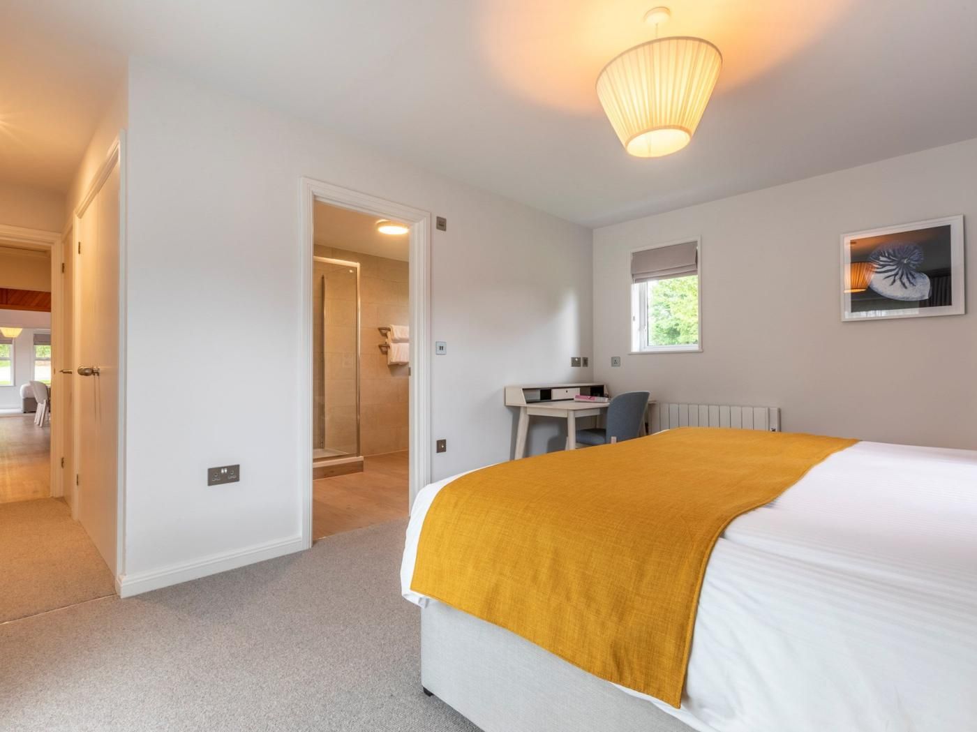 Ein Hotelzimmer mit einem Bett, einem Schreibtisch, einem Sessel, einem Fenster und einer Tür zu einem weiteren Raum.