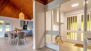 Une cuisine moderne avec un plafond en bois, un coin repas avec des chaises et une porte vitrée donnant sur une pièce lumineuse.